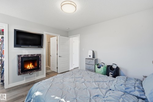 Bedroom featuring a premium fireplace, wood finished floors, a textured ceiling, and connected bathroom - 7803 Yorke Road, Edmonton, AB - Indoor Photo Showing Bedroom With Fireplace