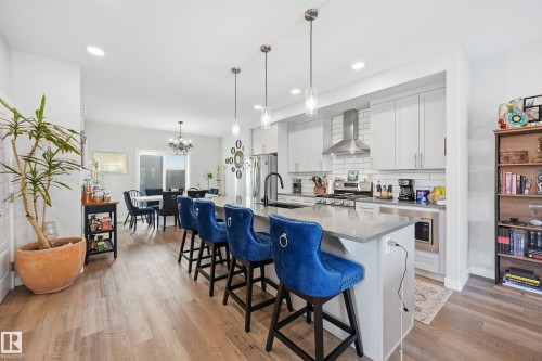 Kitchen featuring white cabinets, a kitchen breakfast bar, wall chimney exhaust hood, an island with sink, and recessed lighting - 7803 Yorke Road, Edmonton, AB - Indoor