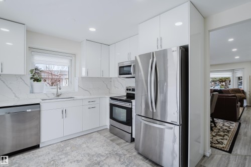 Kitchen with stainless steel appliances, white cabinets, light stone countertops, backsplash, and modern cabinets - 236 Lago Lindo Crescent, Edmonton, AB 