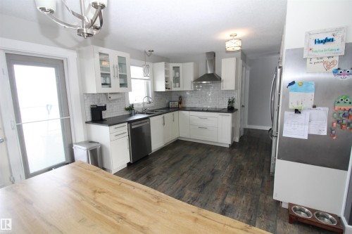 Kitchen featuring white cabinets, dark wood-style flooring, glass insert cabinets, stainless steel appliances, and dark countertops - 10319 106 Ave, Westlock, AB - Indoor Photo Showing Kitchen With Double Sink