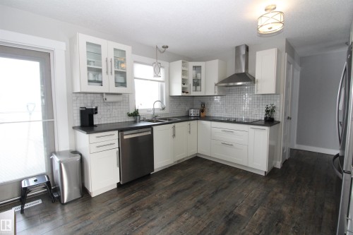 Kitchen featuring stainless steel appliances, dark wood-style floors, white cabinetry, dark countertops, and glass fronted cabinets - 10319 106 Ave, Westlock, AB - Indoor Photo Showing Kitchen With Double Sink With Upgraded Kitchen