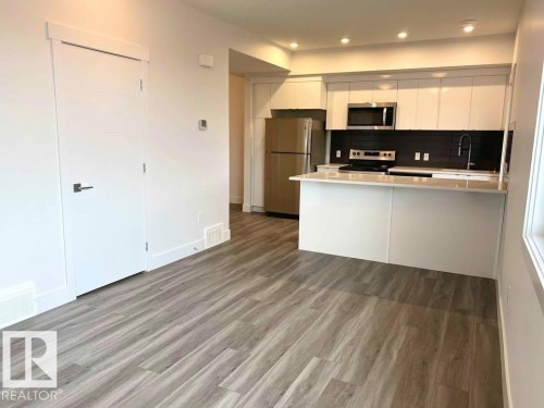 Kitchen featuring white cabinetry, a peninsula, stainless steel appliances, light wood-type flooring, and tasteful backsplash - 10 446 Allard Boulevard, Edmonton, AB - Indoor Photo Showing Kitchen