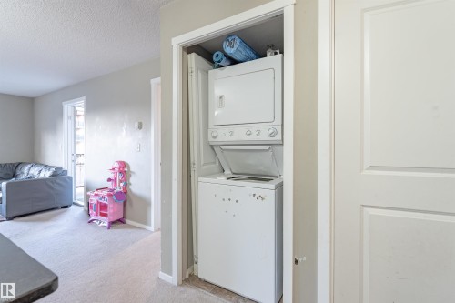 Laundry area with light colored carpet, a textured ceiling, and stacked washer / drying machine - 206 3207 James Mowatt Trail, Edmonton, AB - Indoor Photo Showing Laundry Room