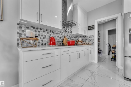 Kitchen featuring white cabinetry, extractor fan, light marble finish flooring, modern cabinets, and stainless steel fridge - 3607 46 Avenue, Beaumont, AB - Indoor Photo Showing Other Room