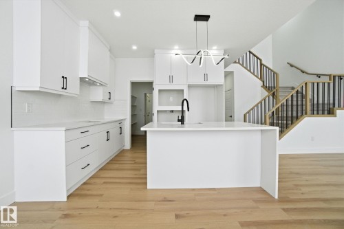 Kitchen with a kitchen island with sink, light wood-style flooring, pendant lighting, and light stone counters - 2408 208 Street, Edmonton, AB - Indoor Photo Showing Kitchen