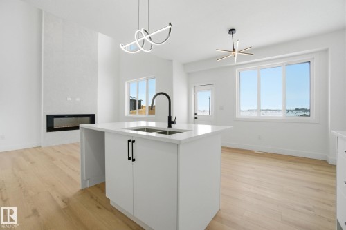 Kitchen with a large fireplace, light wood finished floors, white cabinets, and a kitchen island with sink - 2408 208 Street, Edmonton, AB - Indoor Photo Showing Kitchen With Double Sink