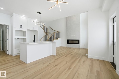 Kitchen featuring white cabinetry, light wood-style flooring, a fireplace, a center island with sink, and open floor plan - 2408 208 Street, Edmonton, AB - Indoor Photo Showing Other Room