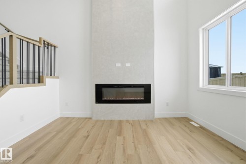Unfurnished living room featuring light wood-type flooring, a glass covered fireplace, and a high ceiling - 2408 208 Street, Edmonton, AB - Indoor Photo Showing Other Room With Fireplace