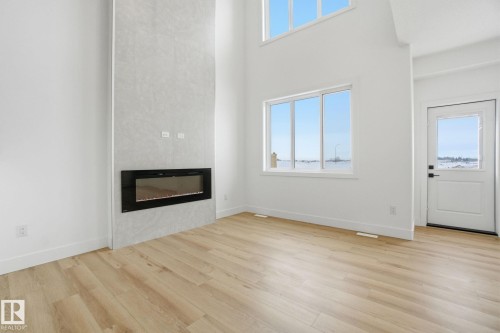 Unfurnished living room featuring a high ceiling, a glass covered fireplace, light wood-type flooring, and healthy amount of natural light - 2408 208 Street, Edmonton, AB - Indoor Photo Showing Other Room With Fireplace