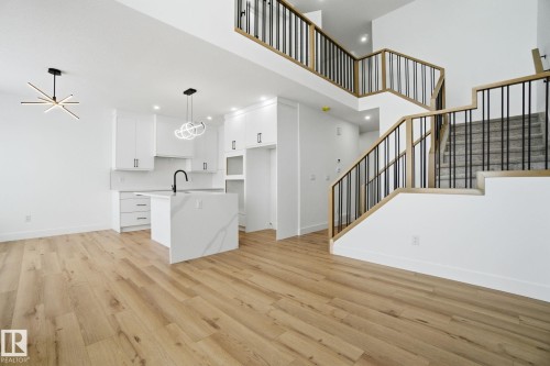 Kitchen with a kitchen island with sink, white cabinetry, open floor plan, light wood finished floors, and a high ceiling - 2408 208 Street, Edmonton, AB - Indoor Photo Showing Other Room