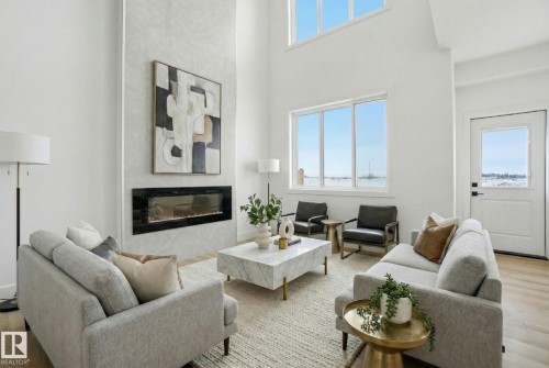 Living area with wood finished floors, a high ceiling, and a glass covered fireplace - 2408 208 Street, Edmonton, AB - Indoor Photo Showing Living Room With Fireplace