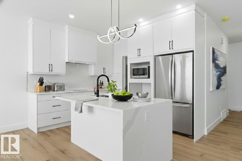 Kitchen with stainless steel appliances, an island with sink, light wood finished floors, tasteful backsplash, and white cabinetry - 2408 208 Street, Edmonton, AB - Indoor Photo Showing Kitchen With Upgraded Kitchen