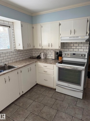 Kitchen with white range with electric stovetop, decorative backsplash, white cabinetry, and ornamental molding - 4506 53 Avenue, Barrhead, AB - Indoor Photo Showing Kitchen