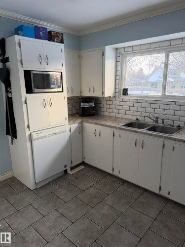 Kitchen with white cabinets, backsplash, dishwasher, ornamental molding, and stainless steel microwave - 4506 53 Avenue, Barrhead, AB - Indoor Photo Showing Kitchen With Double Sink