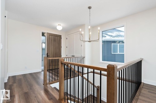 Hallway with an upstairs landing, dark wood-type flooring, and hanging lights - 128 Lilac Close, Leduc, AB 