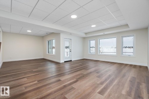 Unfurnished living room with plenty of natural light, dark wood-style flooring, a tray ceiling, and a paneled ceiling - 128 Lilac Close, Leduc, AB 