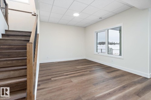 Stairway featuring a drop ceiling and wood finished floors - 128 Lilac Close, Leduc, AB 