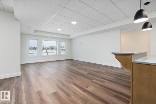 Unfurnished living room with dark wood finished floors, a raised ceiling, and a drop ceiling - 128 Lilac Close, Leduc, AB 