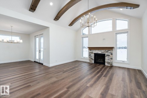 Unfurnished living room with hanging lights, vaulted ceiling, dark wood-style flooring, and a stone fireplace - 128 Lilac Close, Leduc, AB 