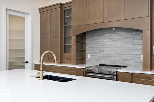 Kitchen featuring stainless steel range with electric stovetop, glass insert cabinets, light stone countertops, and decorative backsplash - 128 Lilac Close, Leduc, AB 