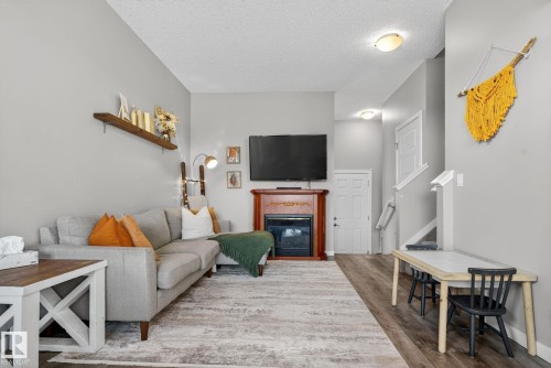 Living area featuring a textured ceiling, wood finished floors, and a glass covered fireplace - 211 Sturtz Bend, Leduc, AB - Indoor Photo Showing Living Room With Fireplace