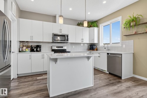 Kitchen featuring white cabinetry, stainless steel appliances, hanging light fixtures, a kitchen bar, and light wood-type flooring - 211 Sturtz Bend, Leduc, AB - Indoor Photo Showing Kitchen With Stainless Steel Kitchen
