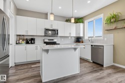 Kitchen featuring white cabinetry, stainless steel appliances, hanging light fixtures, a kitchen bar, and light wood-type flooring - 