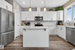 Kitchen featuring stainless steel appliances, white cabinets, decorative light fixtures, and dark wood-type flooring - 