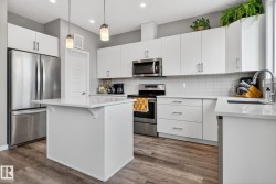 Kitchen with stainless steel appliances, a kitchen island, white cabinetry, hanging light fixtures, and light stone countertops - 