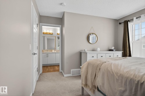 Bedroom featuring light colored carpet, a textured ceiling, and connected bathroom - 211 Sturtz Bend, Leduc, AB - Indoor Photo Showing Bedroom