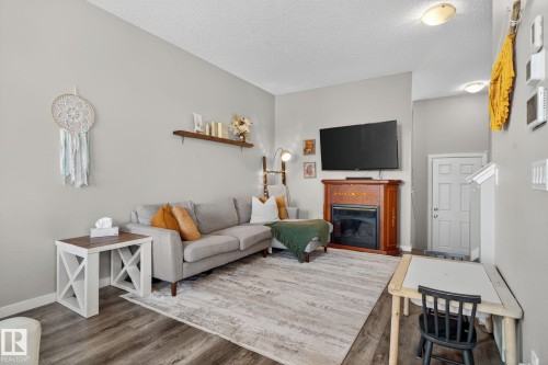 Living area featuring a glass covered fireplace, wood finished floors, and a textured ceiling - 211 Sturtz Bend, Leduc, AB - Indoor Photo Showing Living Room With Fireplace
