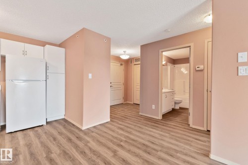 Kitchen with freestanding refrigerator, white cabinetry, light wood finished floors, and a textured ceiling - 406 16035 132 Street Nw, Edmonton, AB - Indoor