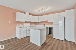 Kitchen featuring white appliances, light countertops, white cabinets, a textured ceiling, and light wood-style floors - 
