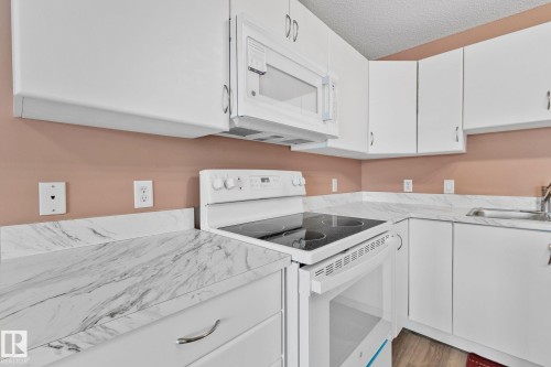 Kitchen with white appliances, white cabinetry, light countertops, a textured ceiling, and wood finished floors - 406 16035 132 Street Nw, Edmonton, AB - Indoor Photo Showing Kitchen