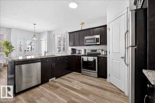 Kitchen featuring stainless steel appliances, hanging light fixtures, a peninsula, light wood finished floors, and light stone countertops - 12761 119 St, Edmonton, AB - Indoor Photo Showing Kitchen