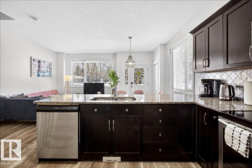 Kitchen featuring open floor plan, a peninsula, stainless steel appliances, dark wood finish cabinets, and a textured ceiling - 12761 119 St, Edmonton, AB - Indoor Photo Showing Kitchen With Double Sink