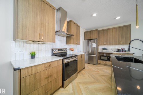 Kitchen with stainless steel appliances, dark stone countertops, wood finish cabinets, parquet flooring, and decorative light fixtures - 15 Chambery Crescent, St. Albert, AB - Indoor Photo Showing Kitchen