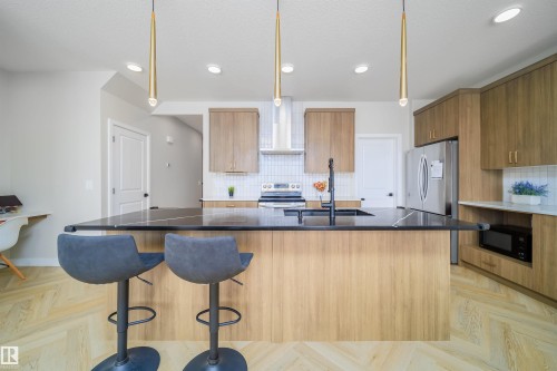 Kitchen featuring modern cabinets, parquet flooring, an island with sink, decorative light fixtures, and stainless steel appliances - 15 Chambery Crescent, St. Albert, AB - Indoor Photo Showing Kitchen