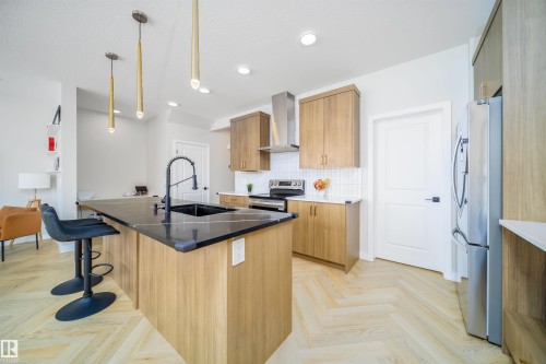 Kitchen featuring an island with sink, stainless steel appliances, parquet floors, decorative light fixtures, and backsplash - 15 Chambery Crescent, St. Albert, AB - Indoor Photo Showing Kitchen With Upgraded Kitchen