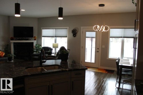 Kitchen with decorative light fixtures, dark stone counters, a fireplace, dark wood-type flooring, and open floor plan - 22 6519 46 Street, Wetaskiwin, AB - Indoor With Fireplace