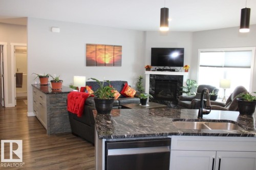 Kitchen with white cabinetry, dark stone countertops, open floor plan, a premium fireplace, and dishwasher - 22 6519 46 Street, Wetaskiwin, AB - Indoor With Fireplace