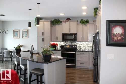 Kitchen with black appliances, dark stone countertops, decorative light fixtures, a breakfast bar, and dark wood-style flooring - 22 6519 46 Street, Wetaskiwin, AB - Indoor Photo Showing Kitchen With Upgraded Kitchen