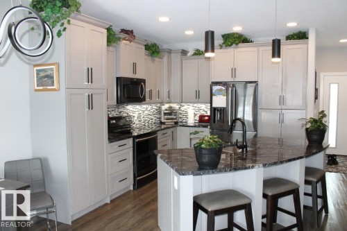 Kitchen with stainless steel appliances, dark stone counters, a breakfast bar, and dark wood-style flooring - 22 6519 46 Street, Wetaskiwin, AB - Indoor Photo Showing Kitchen With Upgraded Kitchen