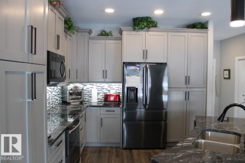 Kitchen with stainless steel appliances, dark stone counters, tasteful backsplash, dark wood-type flooring, and recessed lighting - 22 6519 46 Street, Wetaskiwin, AB - Indoor Photo Showing Kitchen With Double Sink With Upgraded Kitchen
