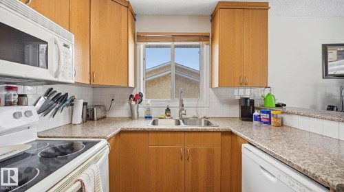 Kitchen featuring white appliances, wood finish cabinetry, light countertops, decorative backsplash, and a textured ceiling - 4502 50A Avenue, Beaumont, AB - Indoor Photo Showing Kitchen With Double Sink