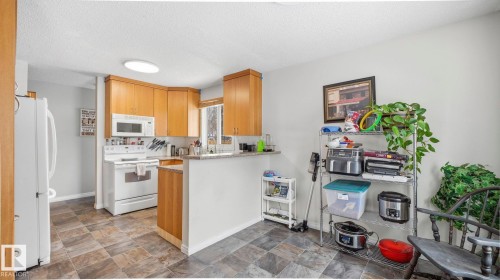 Kitchen featuring stone finish floors, white appliances, a peninsula, a textured ceiling, and backsplash - 4502 50A Avenue, Beaumont, AB - Indoor Photo Showing Kitchen