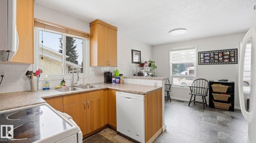 Kitchen featuring white appliances, a peninsula, backsplash, light countertops, and a textured ceiling - 4502 50A Avenue, Beaumont, AB - Indoor Photo Showing Kitchen With Double Sink