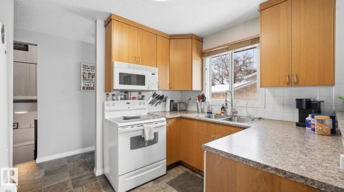 Kitchen with white appliances, decorative backsplash, dark stone finish flooring, light countertops, and a textured ceiling - 4502 50A Avenue, Beaumont, AB - Indoor Photo Showing Kitchen With Double Sink