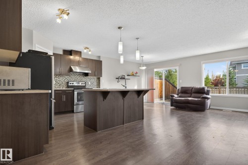 Kitchen featuring a breakfast bar, decorative backsplash, dark wood-style flooring, decorative light fixtures, and stainless steel electric range - 1717 Chapman Way, Edmonton, AB - Indoor Photo Showing Kitchen With Stainless Steel Kitchen With Upgraded Kitchen