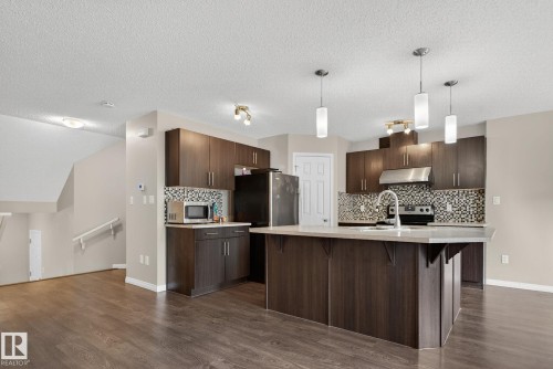 Kitchen with hanging light fixtures, a kitchen breakfast bar, a textured ceiling, decorative backsplash, and dark brown cabinetry - 1717 Chapman Way, Edmonton, AB - Indoor Photo Showing Kitchen With Upgraded Kitchen